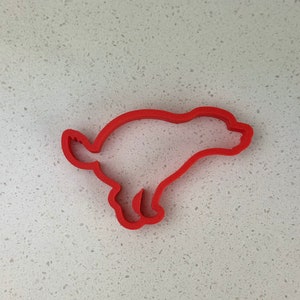 May include: A red plastic cookie cutter shaped like a running dog. The cutter's outline defines the dog's form, including its legs, tail, and body. The design is simple and clean, suitable for baking.