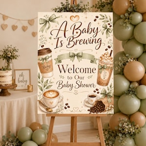 Puede incluir: Un letrero rectangular de bienvenida para baby shower sobre un caballete de madera con el texto A Baby Is Brewing y Welcome to Our Baby Shower. El diseño incluye ilustraciones de tazas de café, granos de café, lazos verdes y follaje.