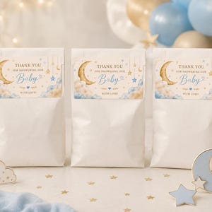 May include: Three white paper favor bags featuring rectangular labels with a gold crescent moon, blue and gold stars, and clouds. The text reads: THANK YOU FOR SHOWERING OUR Baby WITH LOVE! The design includes hanging star ornaments and blue heart accents.