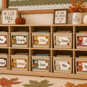 May include: A light wood storage unit with ten beige bins, each featuring a personalized name label with autumn-themed graphics of school supplies and fall leaves. The labels include the names Ava, Brayden, Chloe, Daniel, Emma, Grayson, Harper, Isaac, Mila, and Noah.