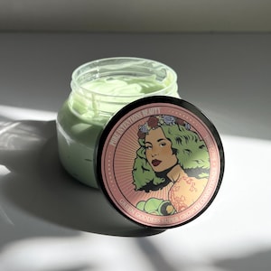 May include: A clear jar filled with a light green cream, with the lid slightly off to the side. The lid features a graphic of a woman with green hair and the text "Green Goddess Super Growth Conditioner."