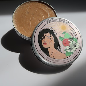 May include: A round, open metal tin containing a light brown balm. The lid, featuring a woman's illustration, reads "PURE INTENTIONS BEAUTY" and "GUAVA CLEANSING BALM". The net weight is 4 oz / 118.2ml. The lid design includes a guava fruit and white flowers.