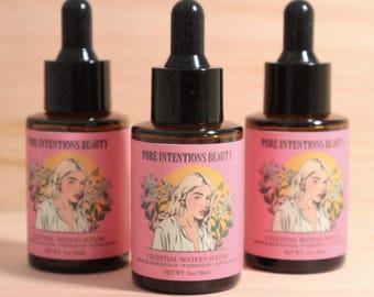 May include: Three amber glass dropper bottles labelled Pure Intentions Beauty Celestial Waters Serum. Each pink label features an illustration of a person with blonde hair surrounded by flowers. The text indicates a net weight of 30ml/1oz.