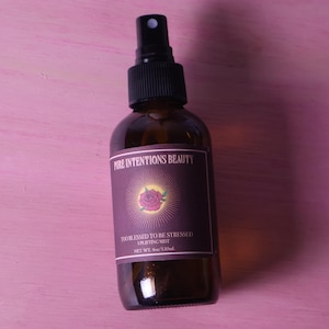 May include: A brown glass bottle with a black spray nozzle. The label reads "PURE INTENTIONS BEAUTY" and "TOO BLESSED TO BE STRESSED UPLIFTING MIST." The bottle contains 4 oz / 120ml of product and features a rose graphic.