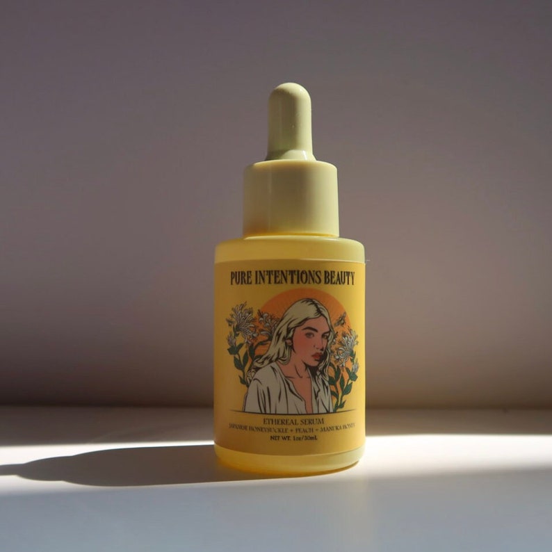 May include: A yellow serum bottle with a dropper. The label reads "Pure Intentions Beauty" and features an illustration of a woman. The bottle also lists ingredients and the text "Ethereal Serum".