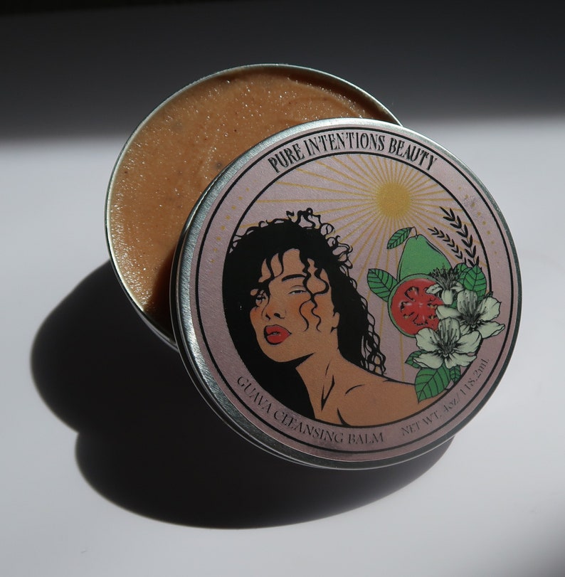 May include: A round metal tin of guava cleansing balm. The lid features a woman's illustration, guava fruit, and the text "Pure Intentions Beauty" and "Guava Cleansing Balm". The balm is a light brown colour and the tin is 118.2ml.