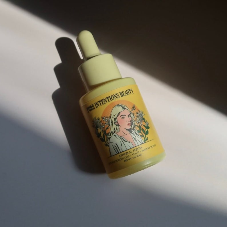 May include: A yellow serum bottle with a dropper, labelled "PURE INTENTIONS BEAUTY." The label features an illustration of a woman and the words "ETHEREAL SERUM." The bottle contains 30ml of product.