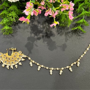 Puede incluir: Un aro de nariz de oro con una cadena de perlas y un colgante decorativo en forma de abanico con piedras blancas.