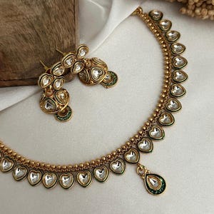 May include: A gold necklace and earrings set with a green and white design. The necklace features a teardrop pendant and heart-shaped stones.