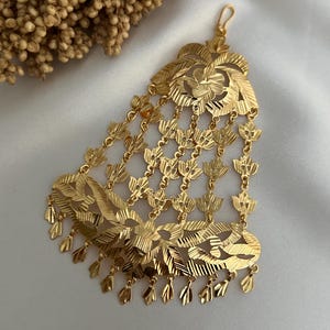 Peut inclure: Un accessoire de cheveux doré orné d'un motif floral. La pièce présente de multiples couches de motifs découpés complexes et des pendentifs en forme de feuilles. L'accessoire est conçu pour être porté sur la tête, probablement pour des occasions spéciales.