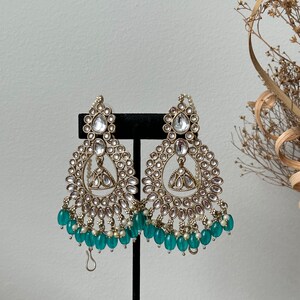 May include: A pair of gold tone earrings with a teardrop shaped design and a fringe of teal beads.