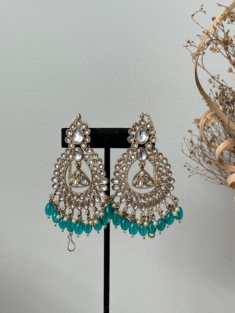 May include: A pair of gold tone earrings with a teardrop shaped design and a fringe of teal beads.