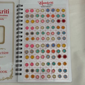 May include: A spiral-bound book of bindis in various colours, including pink, blue, orange, and green. Each bindi has a gold-coloured border. The book is labelled "Janskriti Bindies, Symbol of Beauty."