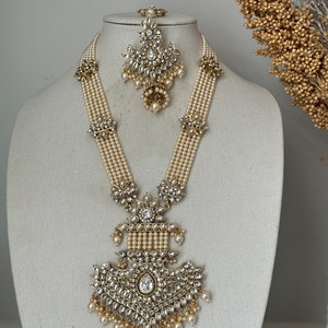 May include: A long, multi-strand pearl necklace with a large, ornate pendant featuring a teardrop-shaped stone and intricate gold detailing. The necklace is paired with a matching, smaller pendant earring.