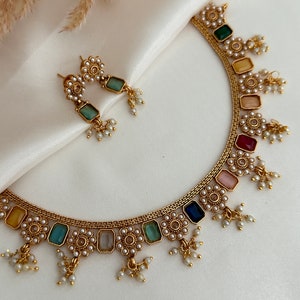 Op de afbeelding: Een gouden ketting met een rij kleurrijke vierkante stenen en parel accenten. De ketting heeft kleine parel druppel accenten. Passende oorbellen met een groene steen en parel accenten.