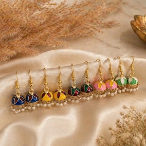 Peut inclure: Une collection de boucles d'oreilles colorées en forme de cloche, avec des crochets dorés et de petits accents de perles. Les boucles d'oreilles présentent diverses combinaisons de couleurs, dont le bleu, le jaune, le rose, le vert et le rouge, avec des motifs complexes.