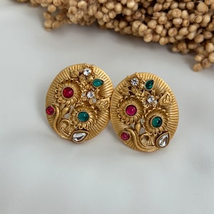 May include: A pair of gold-tone earrings with a floral design. The earrings feature red, green, and white stones.