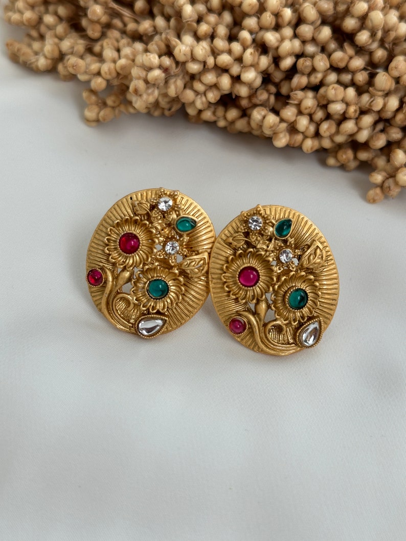 Puede incluir: Un par de pendientes de tono dorado con un dise&ntilde;o floral. Los pendientes presentan piedras rojas, verdes y blancas.