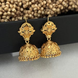 May include: A pair of gold earrings with intricate floral designs and dangling bells. The earrings are made of a shiny, metallic gold.