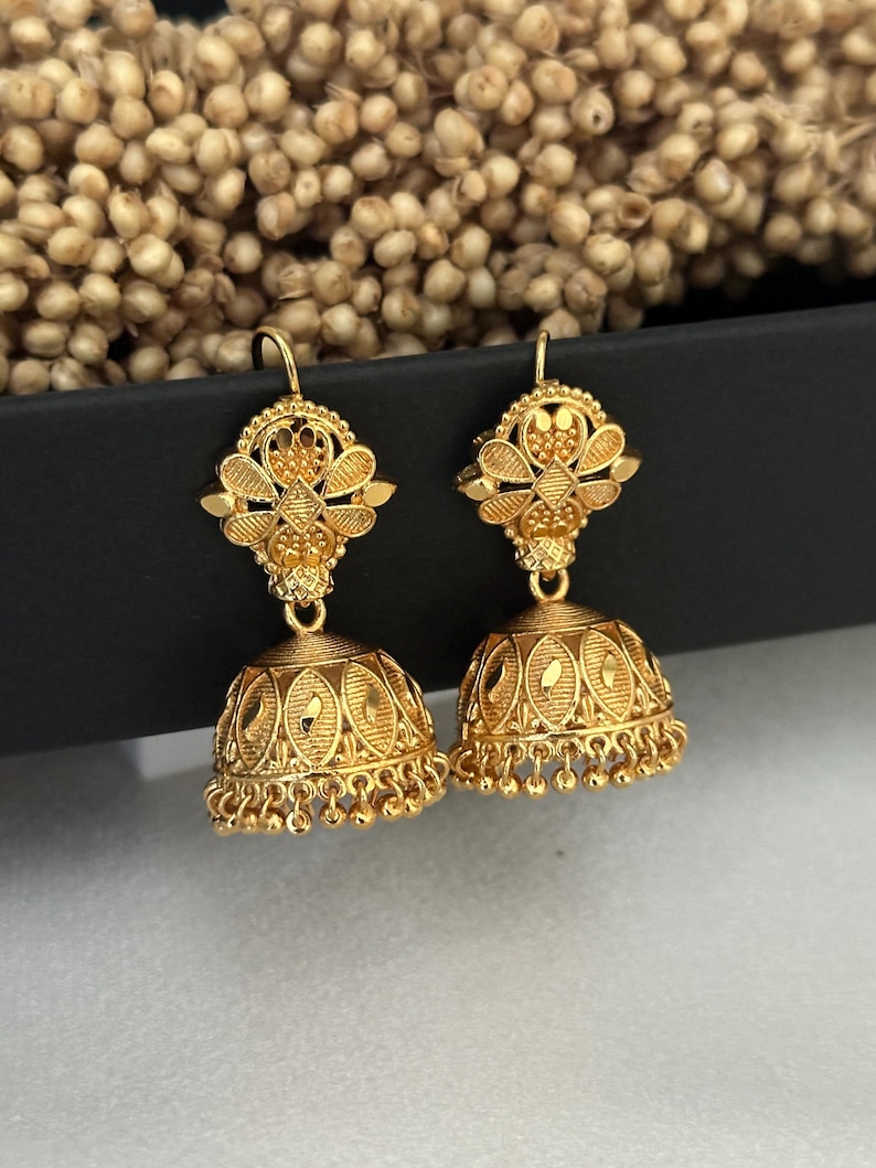 May include: A pair of gold earrings with intricate floral designs and dangling bells. The earrings are made of a shiny, metallic gold.