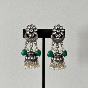 May include: A pair of silver earrings with green and white beads. The earrings have a floral design with a crescent moon shape.