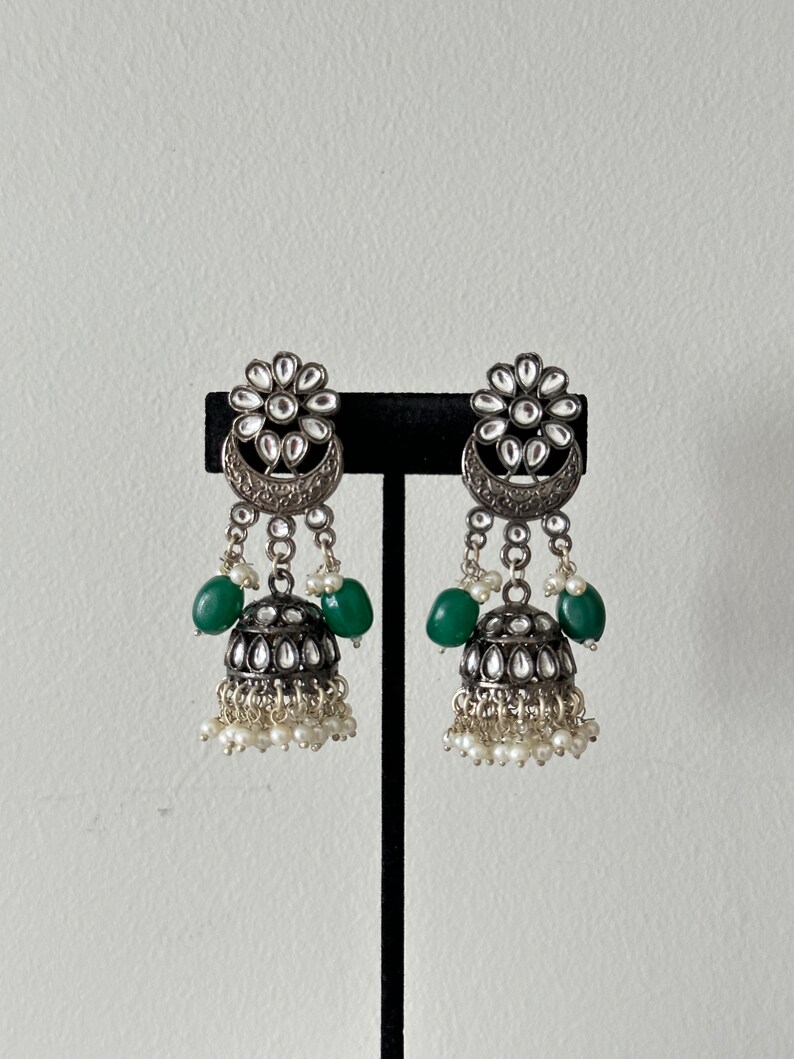 May include: A pair of silver earrings with green and white beads. The earrings have a floral design with a crescent moon shape.