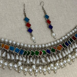 Peut inclure: Un collier en argent avec un motif de carreaux de verre multicolores et des accents de perles blanches. Le collier est assorti d'une paire de boucles d'oreilles avec le m&ecirc;me motif.