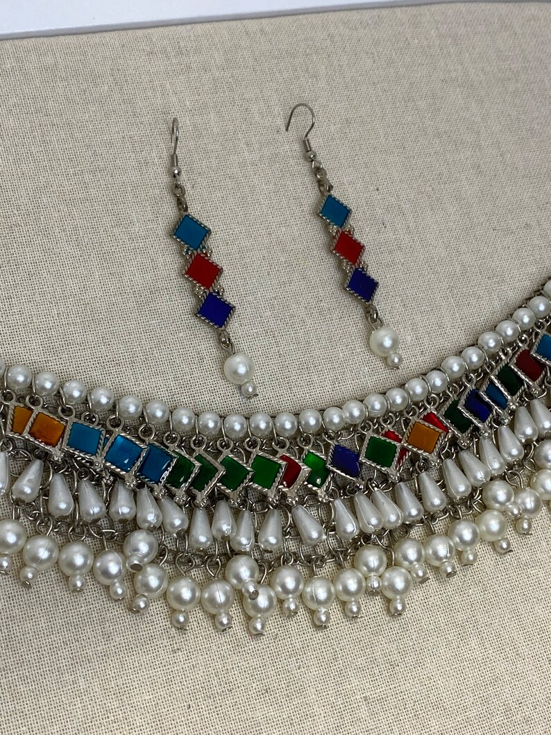 Peut inclure: Un collier en argent avec un motif de carreaux de verre multicolores et des accents de perles blanches. Le collier est assorti d'une paire de boucles d'oreilles avec le m&ecirc;me motif.