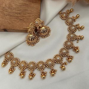 Könnte beinhalten: Ein goldenes Halsketten- und Ohrring-Set mit einem runden Design und kleinen weißen Steinen. Die Halskette hat unten baumelnde Kugeln.