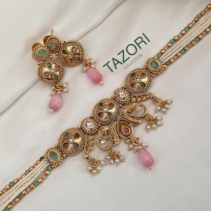 May include: A gold-toned necklace and earring set featuring multi-strand beaded chains in green and pink, accented with circular filigree medallions, clear crystals, small white pearls, and teardrop-shaped pink stones. The text TAZORI COLLECTION is visible.