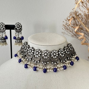 May include: A silver and white choker necklace with blue beads and matching earrings. The necklace features a floral design with pearl accents.