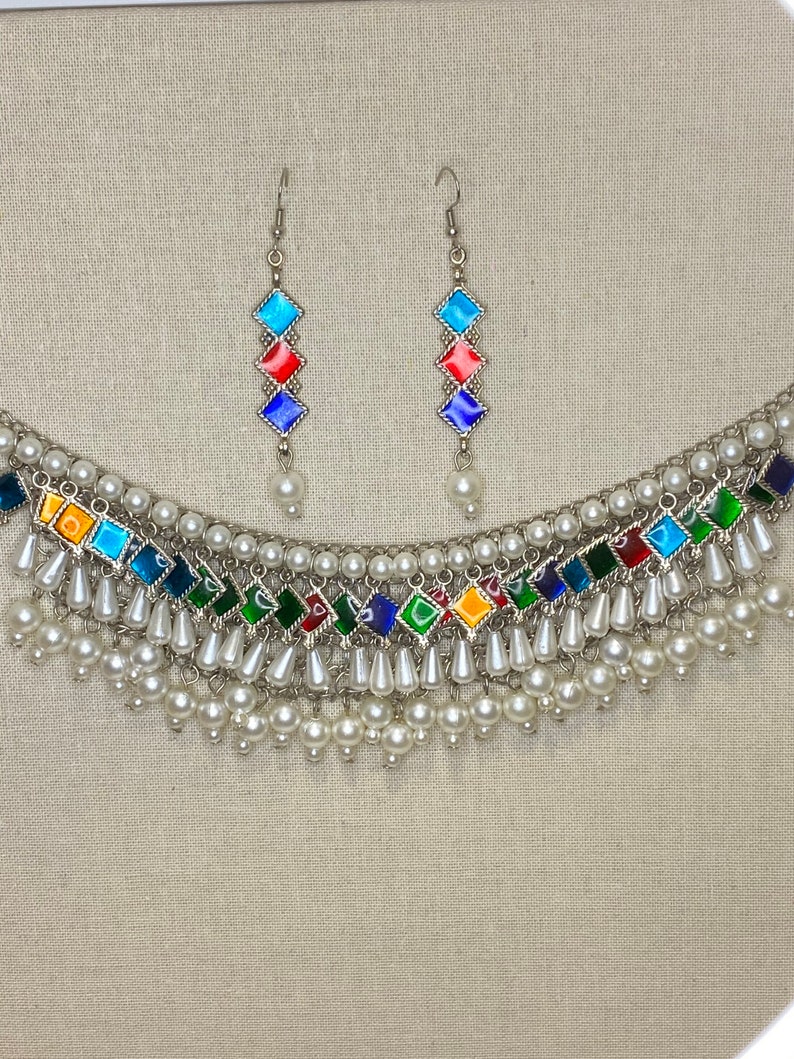 Peut inclure: Un collier en argent avec un motif en &eacute;mail multicolore et des accents de perles blanches. Le collier a un design en couches avec plusieurs rang&eacute;es de perles. Des boucles d'oreilles assorties avec un design en &eacute;mail similaire sont incluses.