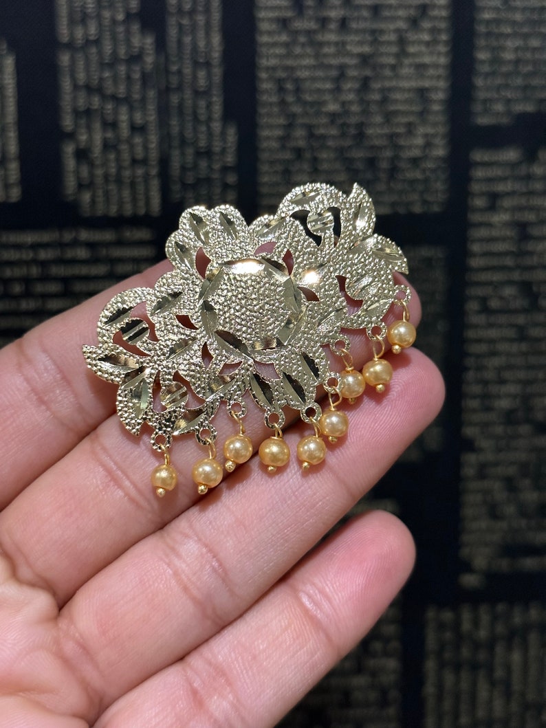 May include: Gold filigree pendant with a floral design and a dangling row of small pearl-like beads.