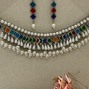 Peut inclure: Un collier en argent avec un motif de carreaux de verre multicolores et des accents de perles blanches. Le collier a un design en couches avec plusieurs rangs de perles. Des boucles d'oreilles assorties avec un design similaire sont &eacute;galement incluses.