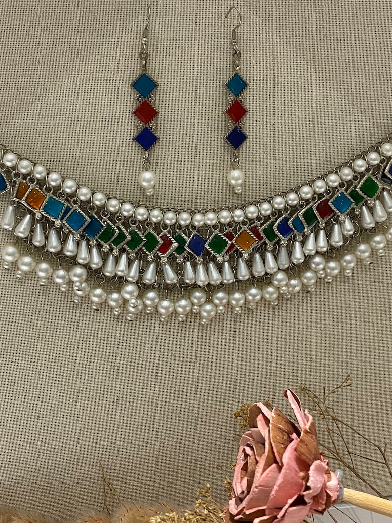 Peut inclure: Un collier en argent avec un motif de carreaux de verre multicolores et des accents de perles blanches. Le collier a un design en couches avec plusieurs rangs de perles. Des boucles d'oreilles assorties avec un design similaire sont &eacute;galement incluses.