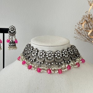 May include: A silver choker necklace with pink and white beads. The necklace features a silver design with floral accents. Matching earrings are also included.