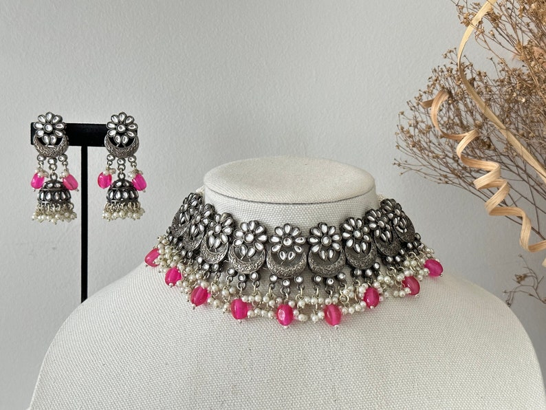 May include: A silver choker necklace with pink and white beads. The necklace features a silver design with floral accents. Matching earrings are also included.