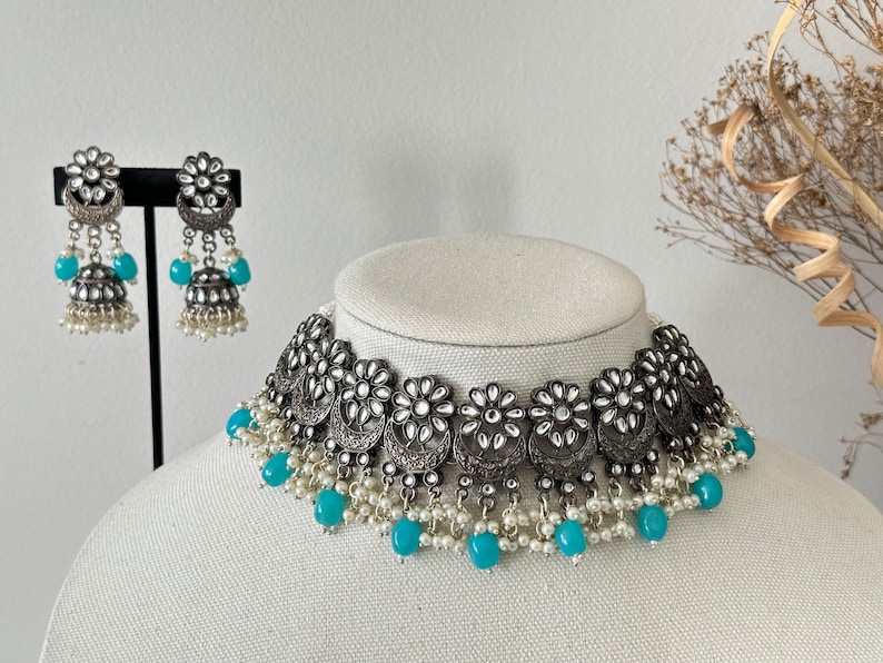 May include: A silver and turquoise choker necklace with a floral design and pearl accents. The necklace is displayed on a mannequin.