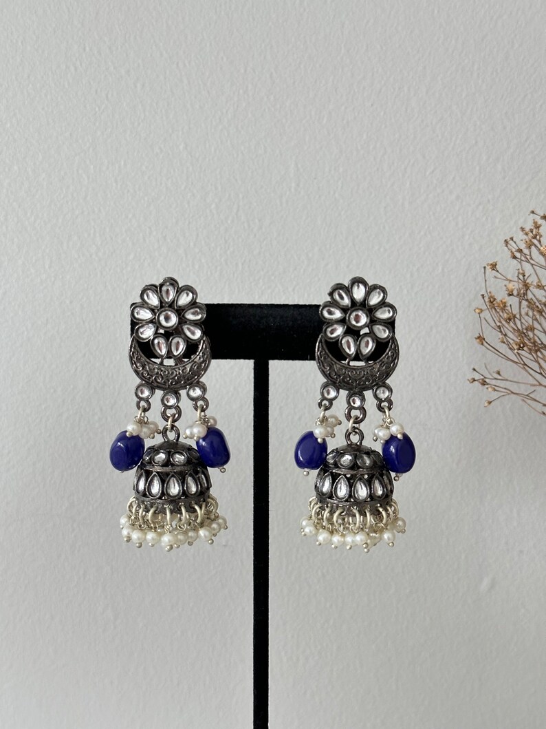 May include: Silver tone earrings with a floral design, blue beads, and white pearl accents.