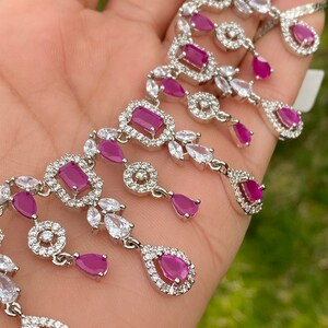 May include: A silver necklace with a delicate design featuring multiple teardrop-shaped pink stones surrounded by smaller clear stones.