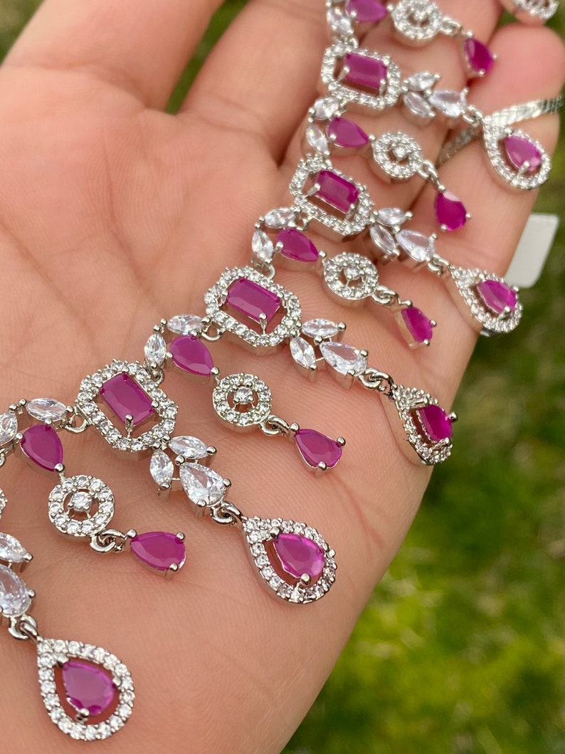 May include: A silver necklace with a delicate design featuring multiple teardrop-shaped pink stones surrounded by smaller clear stones.