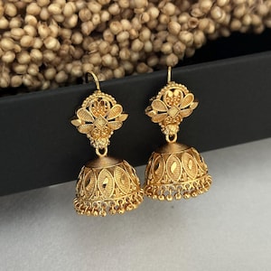 May include: A pair of gold-tone earrings with intricate floral designs. The earrings have a dangling bell-shaped charm with a beaded fringe.