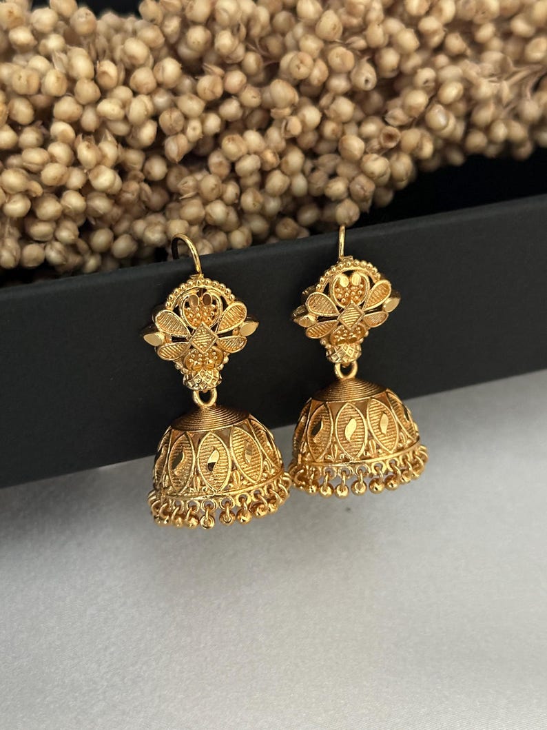 May include: A pair of gold-tone earrings with intricate floral designs. The earrings have a dangling bell-shaped charm with a beaded fringe.
