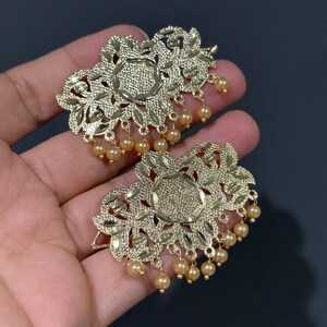 May include: A pair of gold-tone earrings with intricate floral designs and dangling pearl accents.