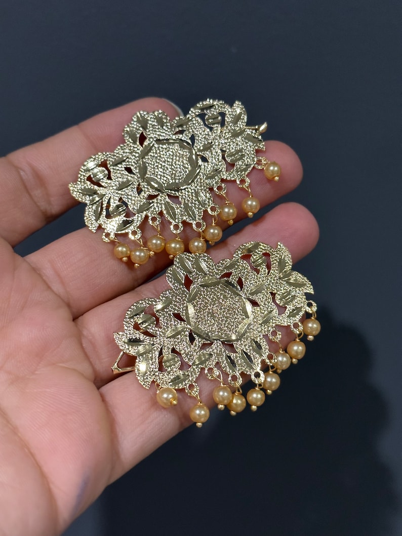 May include: A pair of gold-tone earrings with intricate floral designs and dangling pearl accents.