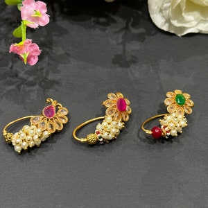 Può includere: Tre anelli per il naso in oro con decorazioni di perle e pietre preziose. Gli anelli presentano una pietra preziosa rosa, rossa e verde al centro di ogni motivo floreale.