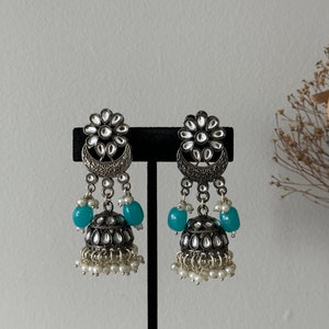May include: A pair of silver earrings with a floral design, blue beads, and pearl accents.