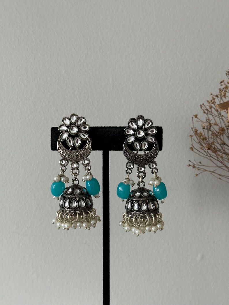 May include: A pair of silver earrings with a floral design, blue beads, and pearl accents.