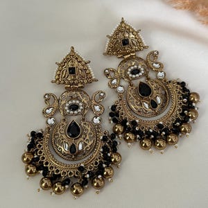 May include: A pair of gold-tone earrings with black and white beads. The earrings feature a crescent moon design with intricate details and black stones.