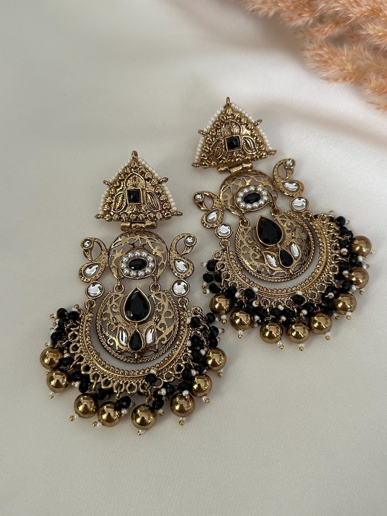 May include: A pair of gold-tone earrings with black and white beads. The earrings feature a crescent moon design with intricate details and black stones.